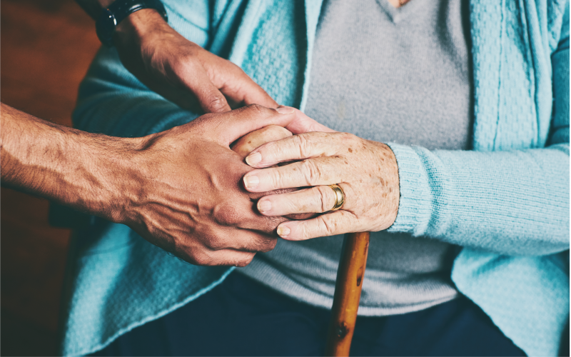 Elderly person holding a carers hand.