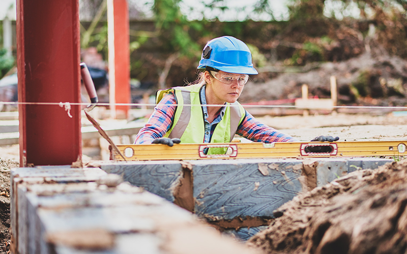 A young female builder using a level to build and check a wall