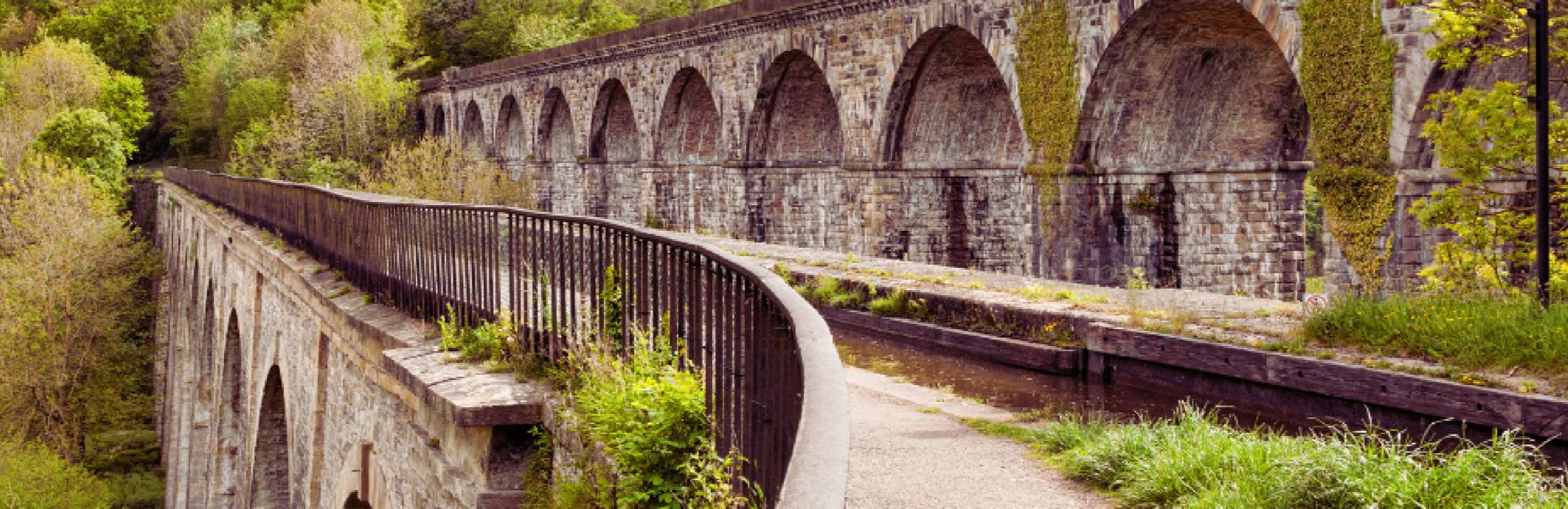 Traphont garreg â bwâu yn Wrecsam, wedi’i hamgylchynu gan wyrddni a llwybr gyda rheiliau.