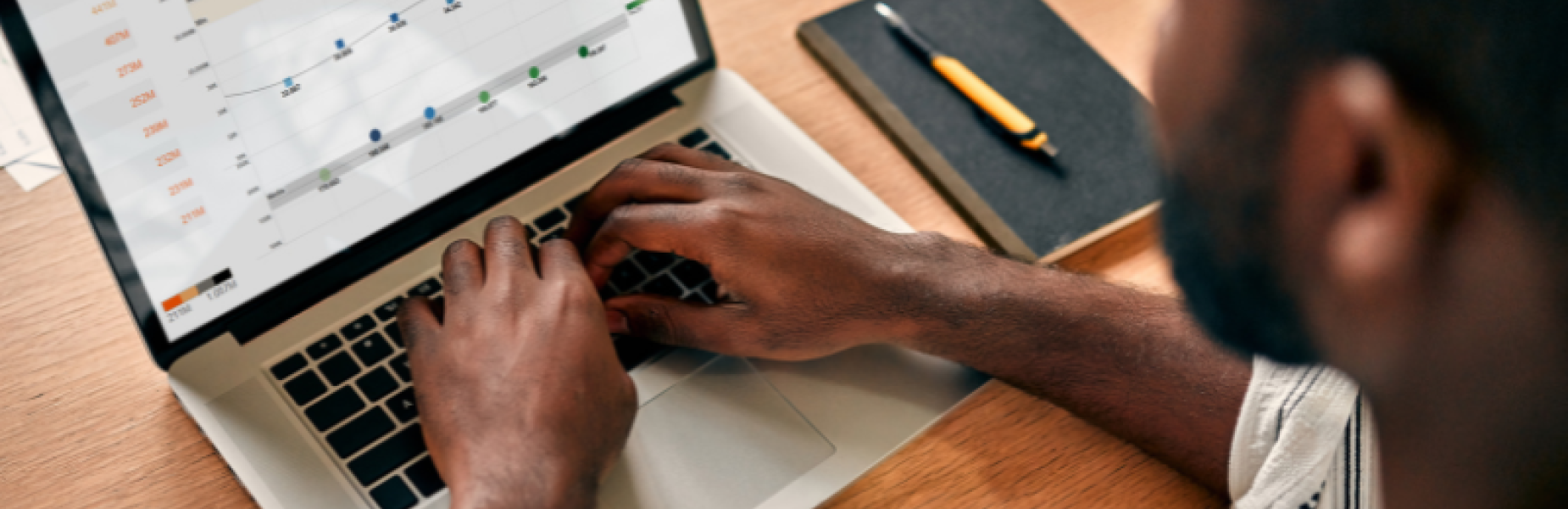 Person using a laptop to review data trends and performance metrics displayed in a line graph on screen. Person yn defnyddio gliniadur i adolygu tueddiadau data a metrigau perfformiad sy'n cael eu dangos mewn graff llinell ar y sgrin.